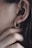 A close-up of an ear adorned with a gold, textured hoop earring resembling a coiled snake. Fingers gently touch the area near the earring, emphasizing the jewelry's intricate details and the texture of the skin.