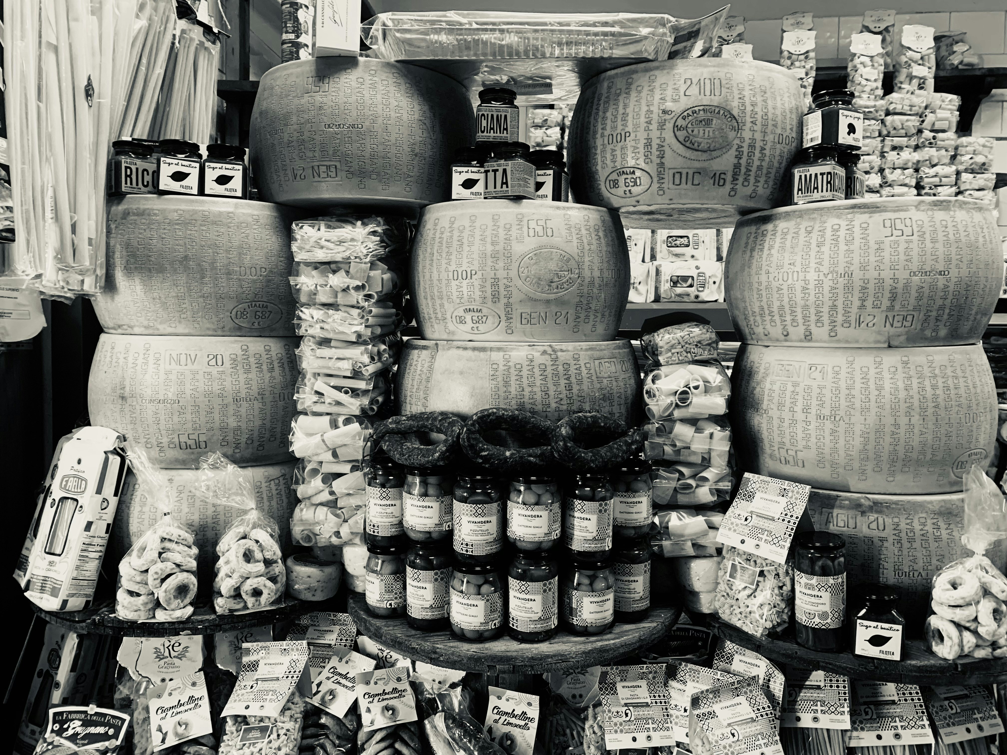 a display in a store filled with lots of cheese, Wall of cheese Parmigiano Reggiano Parmesan cheese wheel Napoli lane shopping Cheese wheel Black and White photography Monochrome