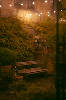 A cozy patio scene featuring a wooden outdoor bar table set surrounded by lush greenery.