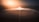 A vast array of solar panels is arranged in concentric circles around a central tower with a bright light, likely depicting a solar power plant. The setting appears to be a desert with a hazy sunrise or sunset casting an orange glow across the landscape.