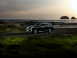 A sleek SUV parked on a sunlit coastal road with turquoise lagoon in the background.