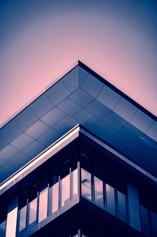 A modern architectural structure with angular lines and reflective glass windows. The building features a prominent roof overhang with a sleek, geometric design. The image has a stylized color palette, adding an artistic flair.