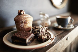 A rustic wooden table displaying muffins with flower-inspired icing in ivory and chocolate brown tones.