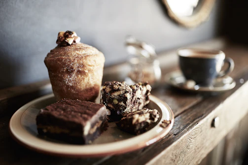 A rustic wooden table displaying muffins with flower-inspired icing in ivory and chocolate brown tones.
