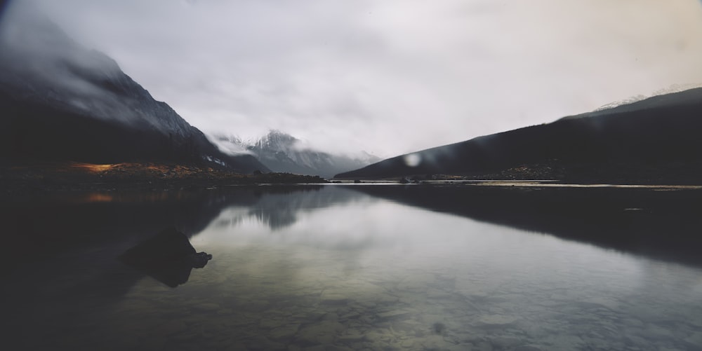 a body of water surrounded by mountains under a cloudy sky