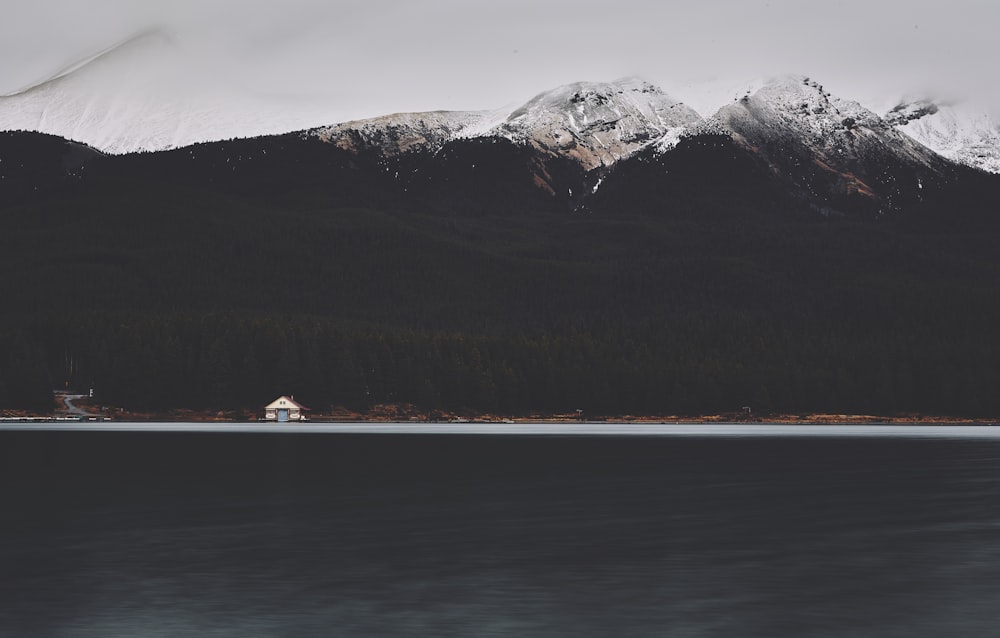 a house on the shore of a lake with mountains in the background