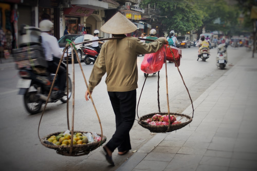 a man walking down a street carrying two baskets of fruit