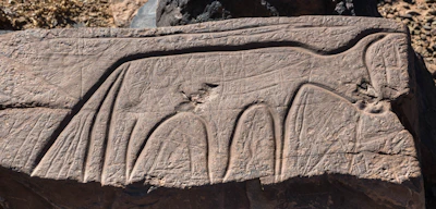 Ancient Harappan seal carved with animal motifs resting on deep sandstone brown surface.