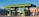 A vibrant green gas station with multiple fuel pumps is situated in a bright area surrounded by motorcycles, a van, and a distinct architectural building with intricate patterns. There are palm trees and flags in the background, adding to the lively and colorful ambiance.