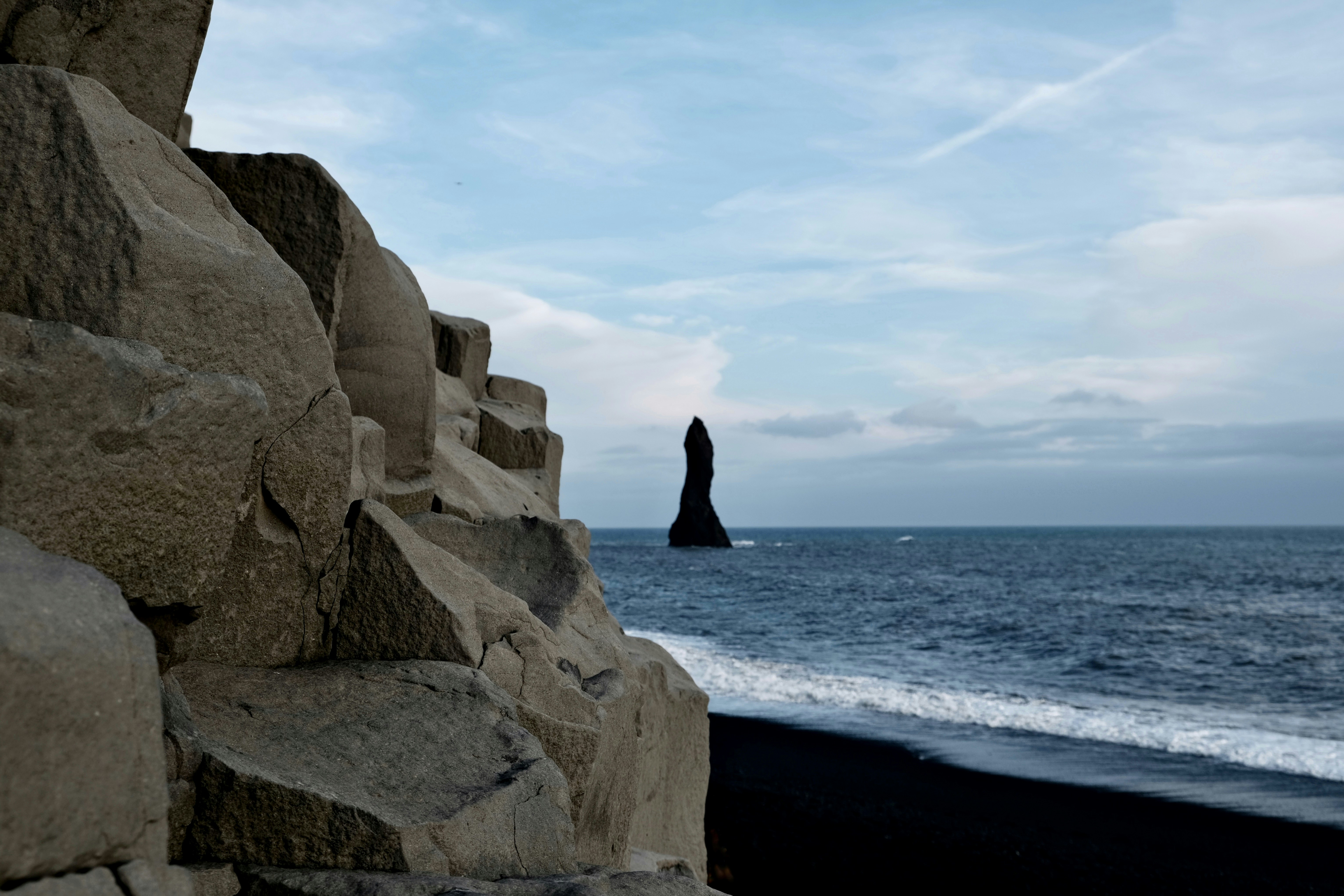 Una playa de arena negra con una formación rocosa en primer plano