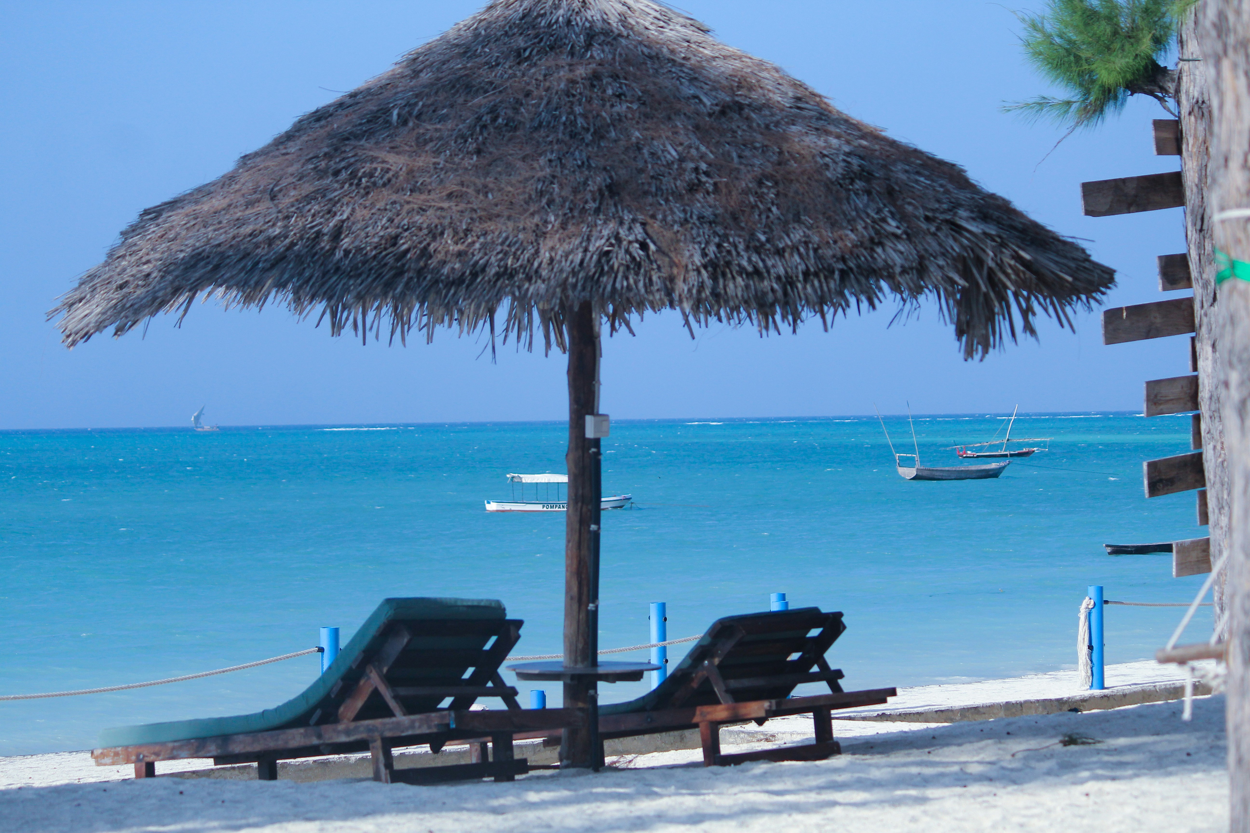 two lounge chairs under a straw umbrella on a beach