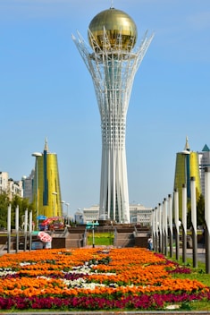 a very tall tower with a golden dome in the middle of a field of flowers
