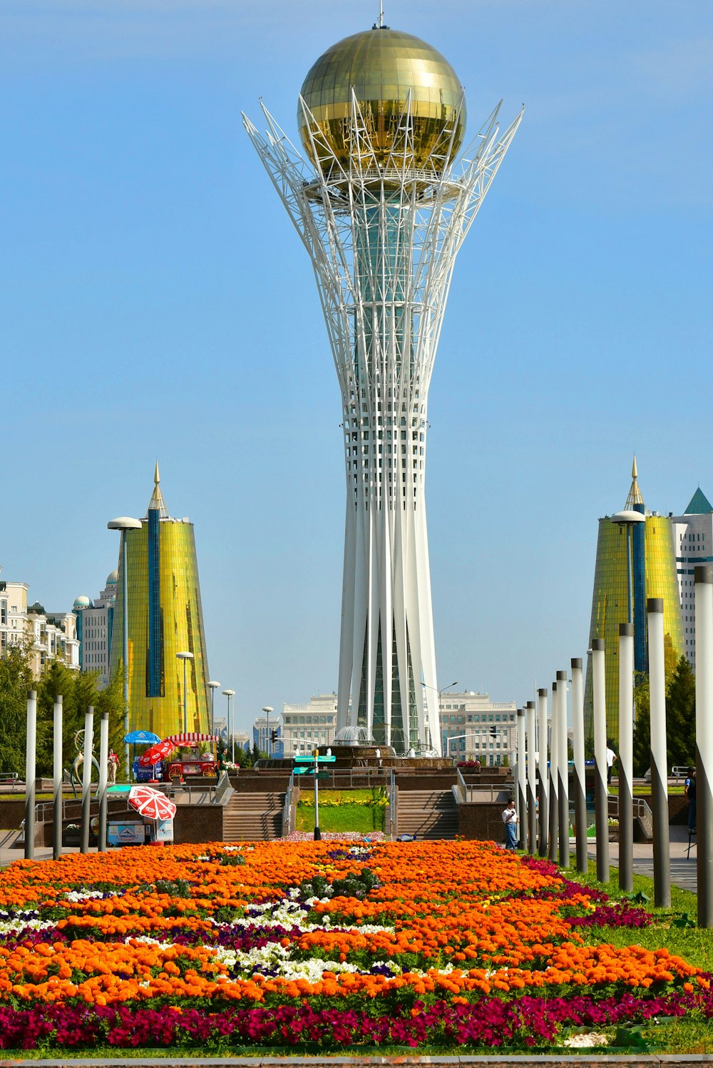 a very tall tower with a golden dome in the middle of a field of flowers