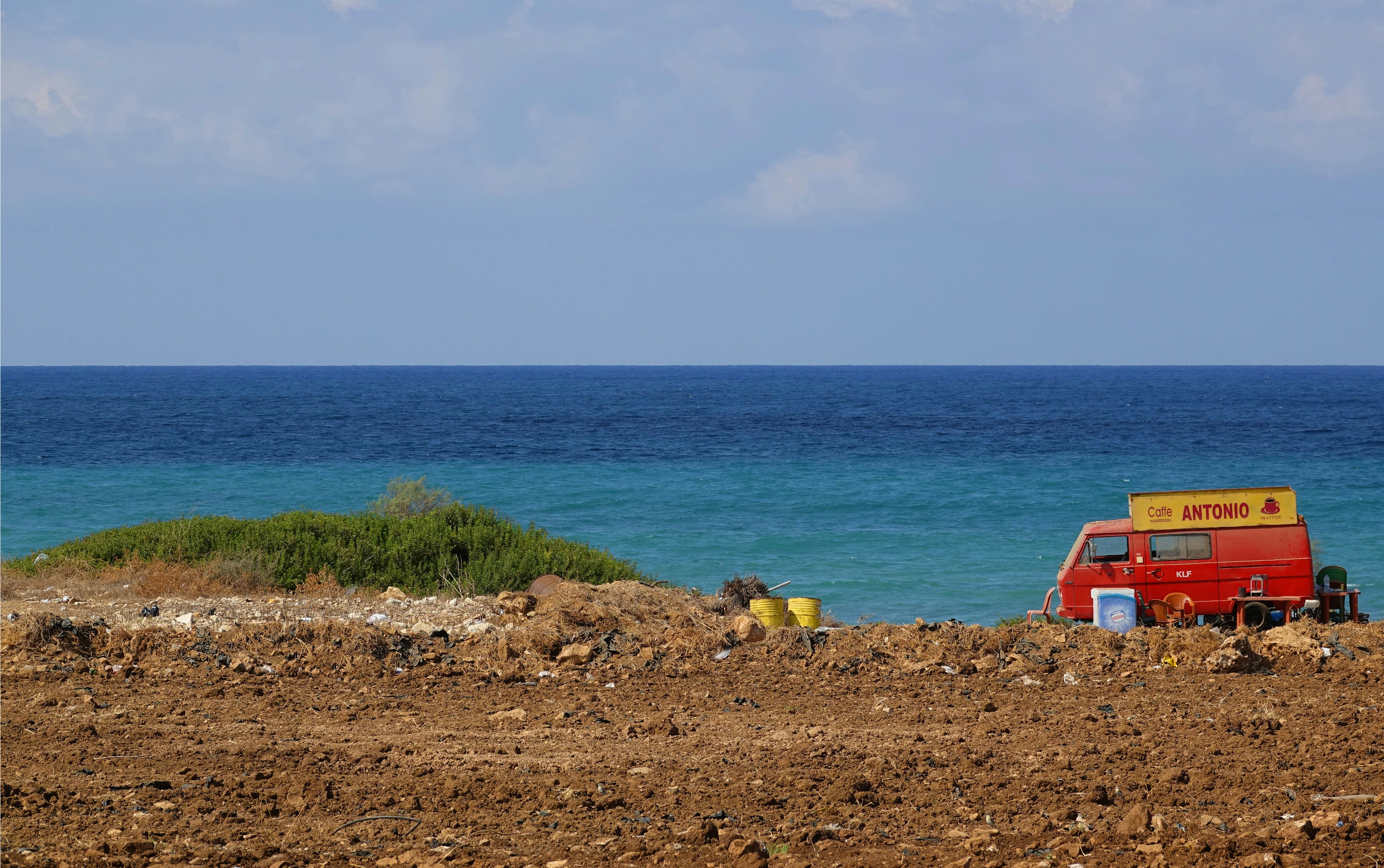 a red van parked on top of a dirt field next to the ocean
