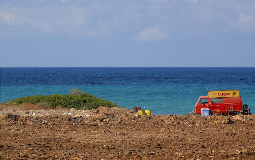 Une camionnette rouge garée au sommet d’un champ de terre au bord de l’océan