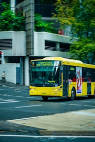a yellow bus driving down a street next to a tall building