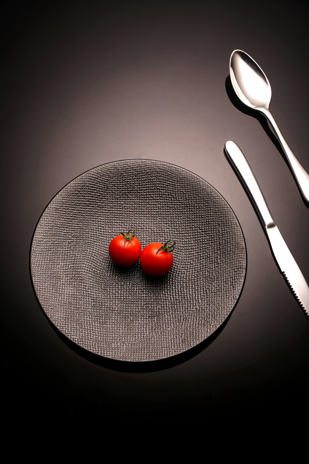 a plate with two tomatoes on it next to a fork and knife