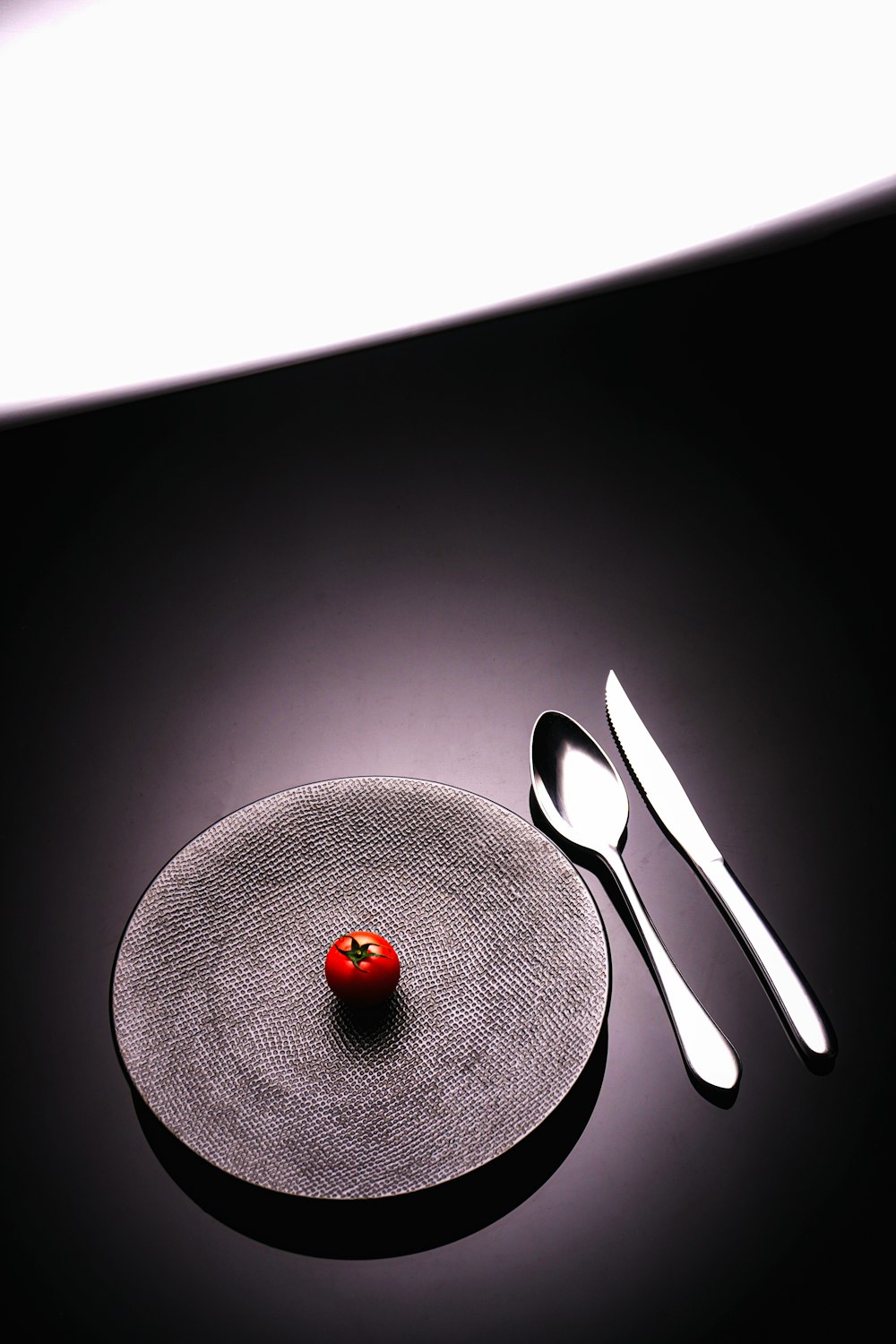 a plate with a fork, knife and a tomato on it