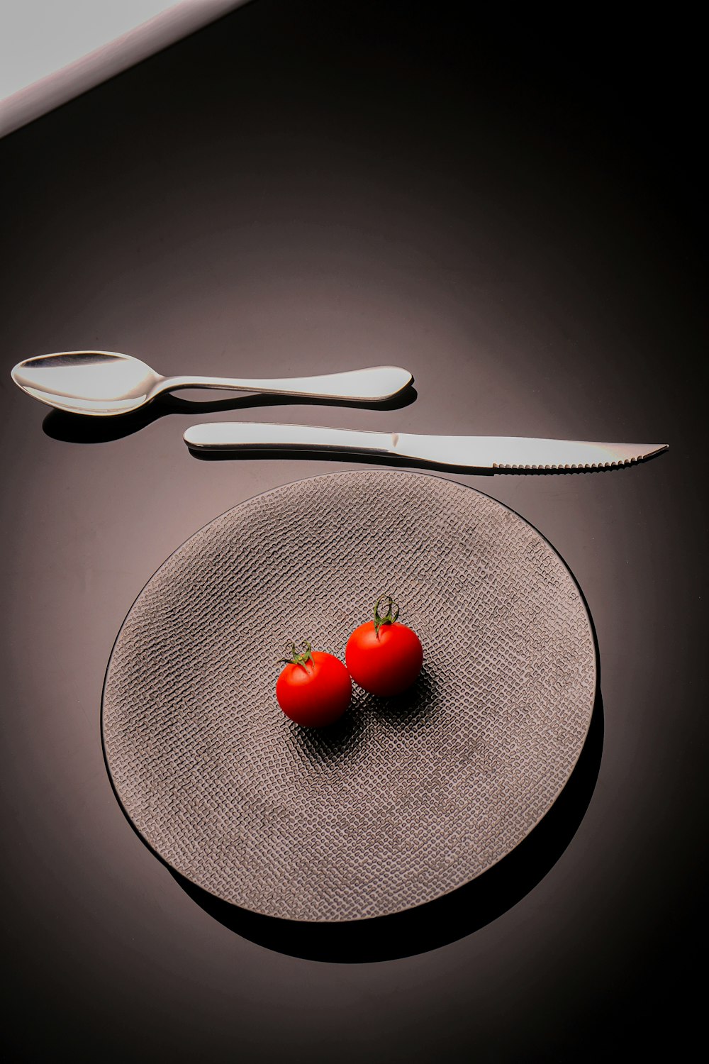 a plate with two tomatoes on it next to a knife and fork