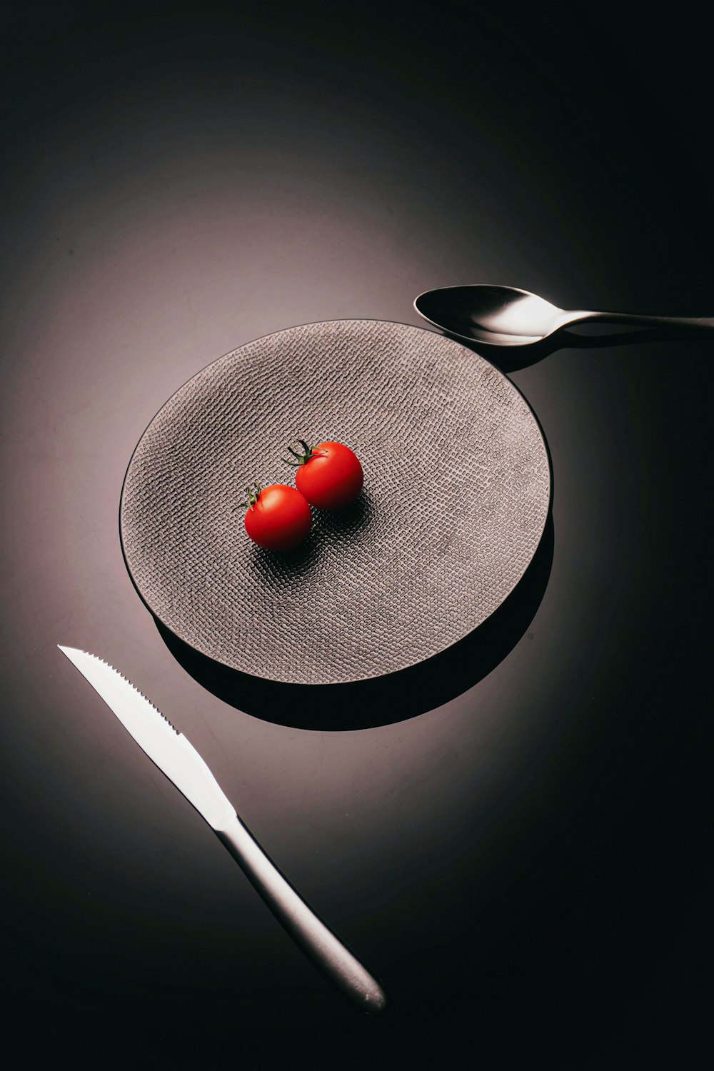 a plate with a tomato on it next to a knife and fork