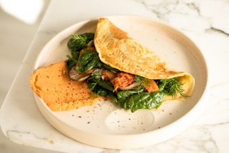 a white plate topped with an omelet and greens