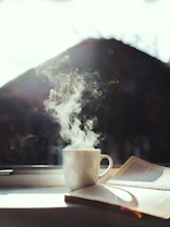 A cozy corner with a steaming cup of coffee beside an open book and soft natural light.
