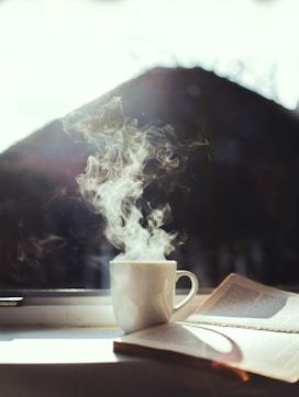 a cup of coffee and a book on a window sill