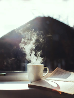 A cozy reading nook with sunlight filtering through a window onto a stack of magazines and a steaming cup of coffee.