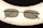 A pair of rectangular framed eyeglasses with dark lenses is centered against a bright, oval-shaped light source, creating a silhouette effect. The frame is thin and metallic, giving a sleek appearance.
