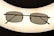 A pair of rectangular framed eyeglasses with dark lenses is centered against a bright, oval-shaped light source, creating a silhouette effect. The frame is thin and metallic, giving a sleek appearance.