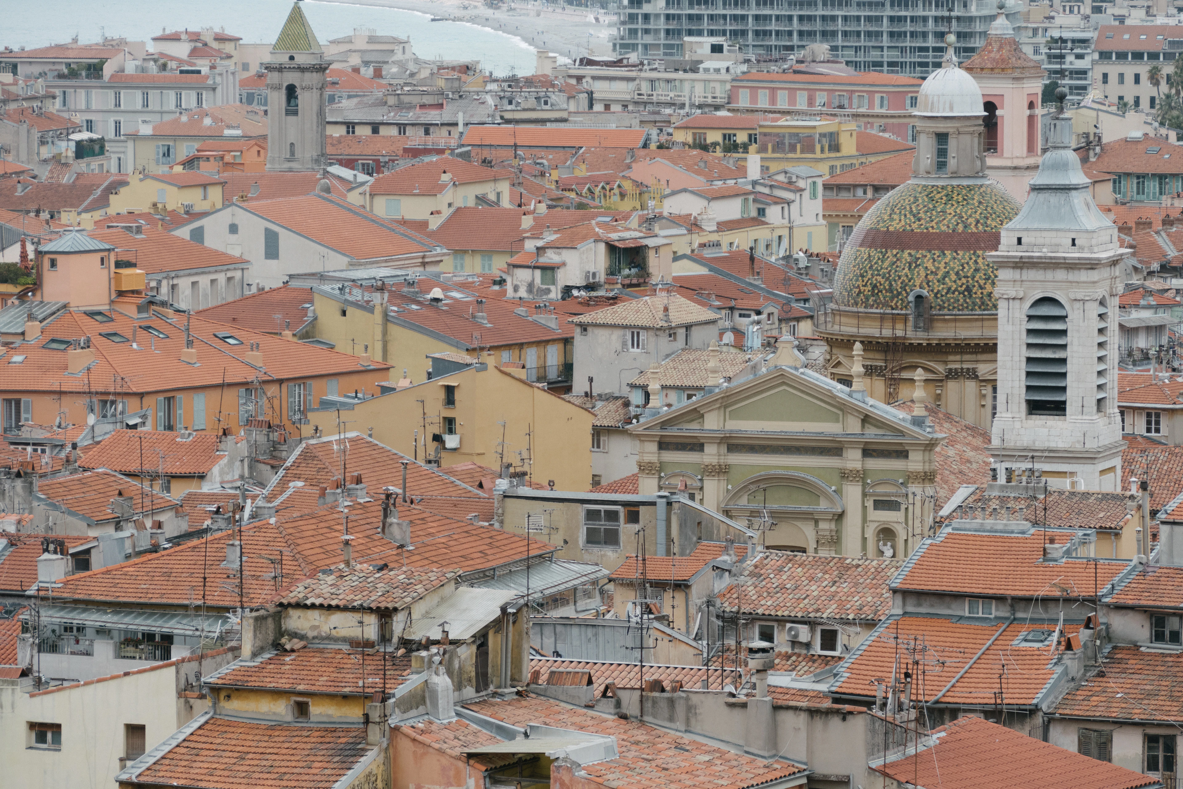 The terracotta rooftops of Vieux Nice seen from Castle Hill, with the tiled dome and white bell tower of the Sainte-Reparate cathedral rising out of the packed old town and the sea beyond.
