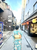 A person wearing a colorful kimono walks down a narrow street lined with traditional buildings and red lanterns. The scene appears peaceful and culturally vibrant, capturing the essence of a historic Japanese setting.