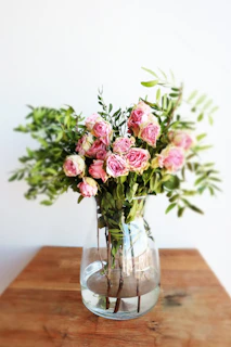 A delicate bouquet of pink and white roses with soft green leaves arranged elegantly on a light wooden table.
