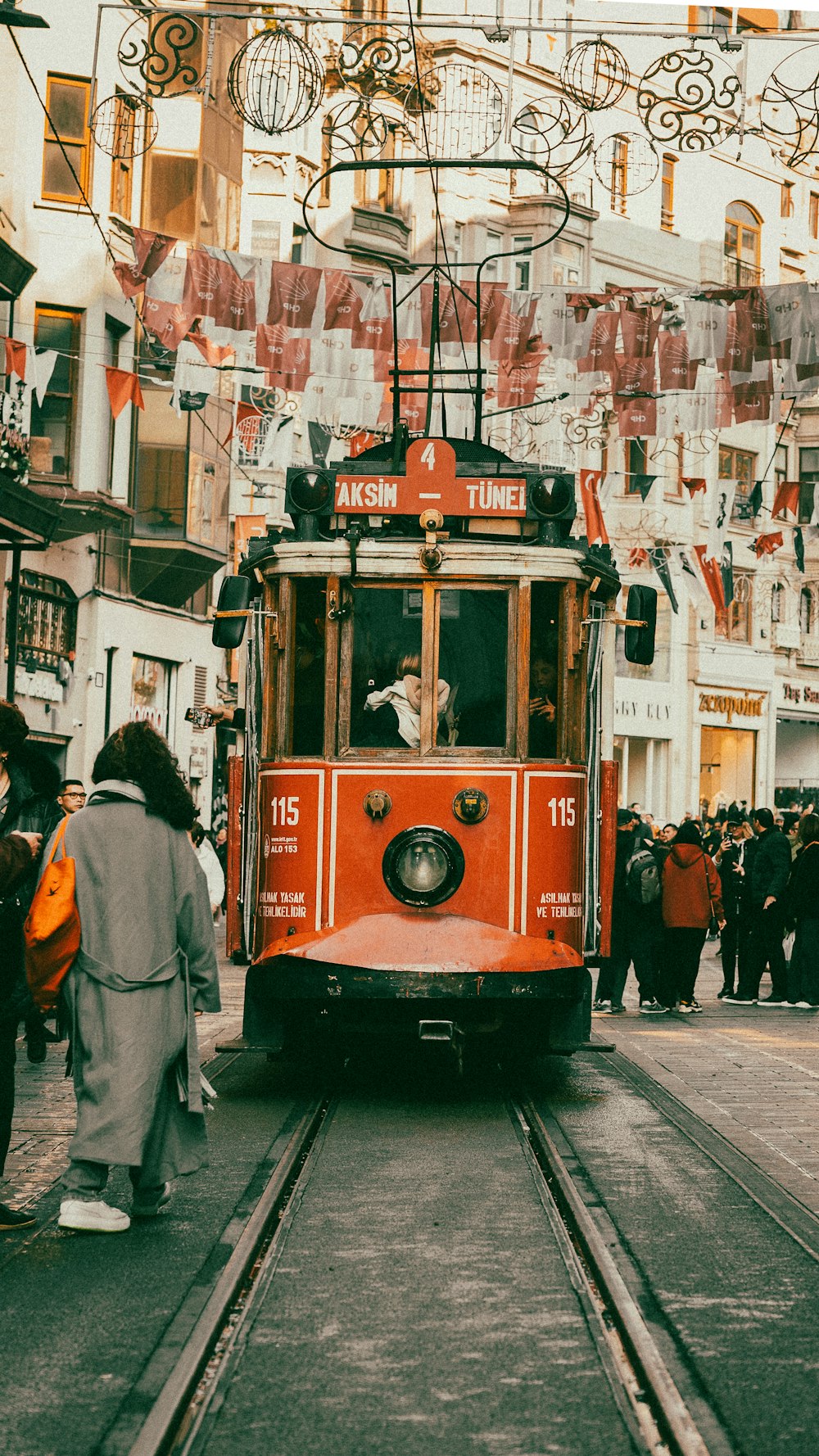 a red trolley car traveling down a street next to a crowd of people