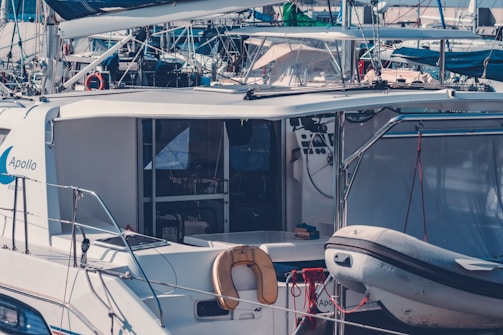 A cluster of boats and yachts at a marina, featuring a close-up on a modern yacht named 'Apollo' with a small inflatable dinghy attached to the side. The boat has a sleek design with various ropes and nautical equipment visible. The scene is packed with other boats in the background, creating a busy and cluttered appearance.