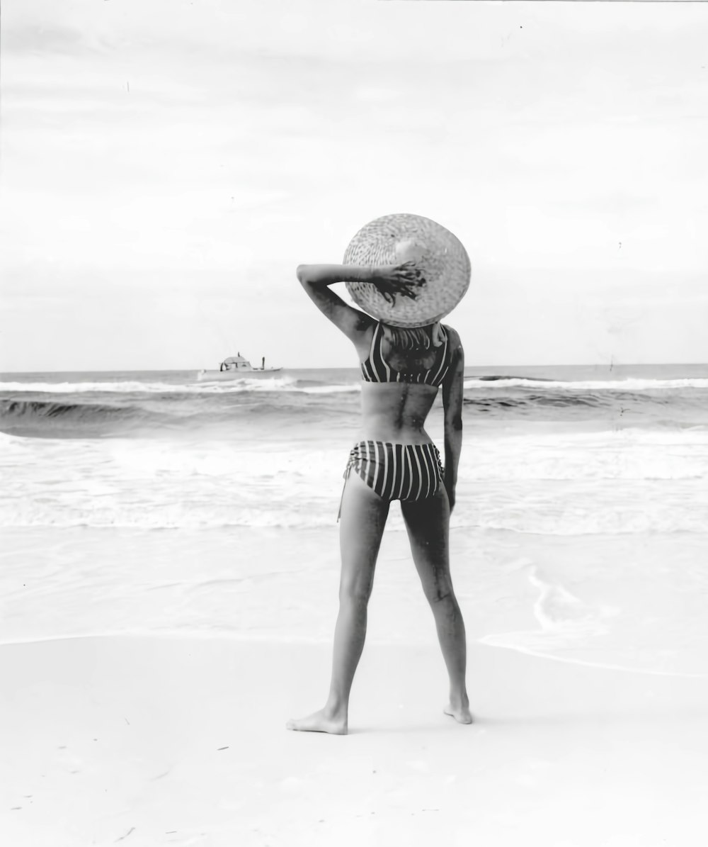 a woman standing on a beach wearing a hat