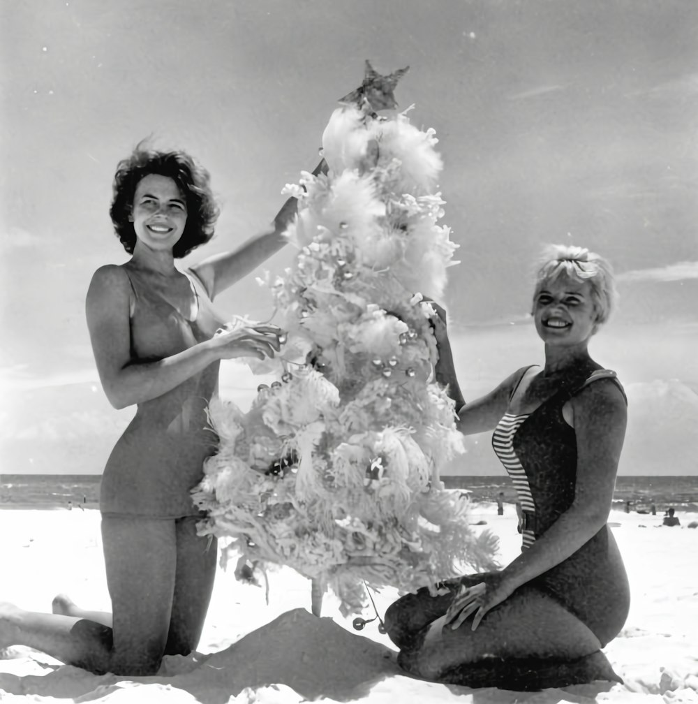 two women are decorating a christmas tree on the beach