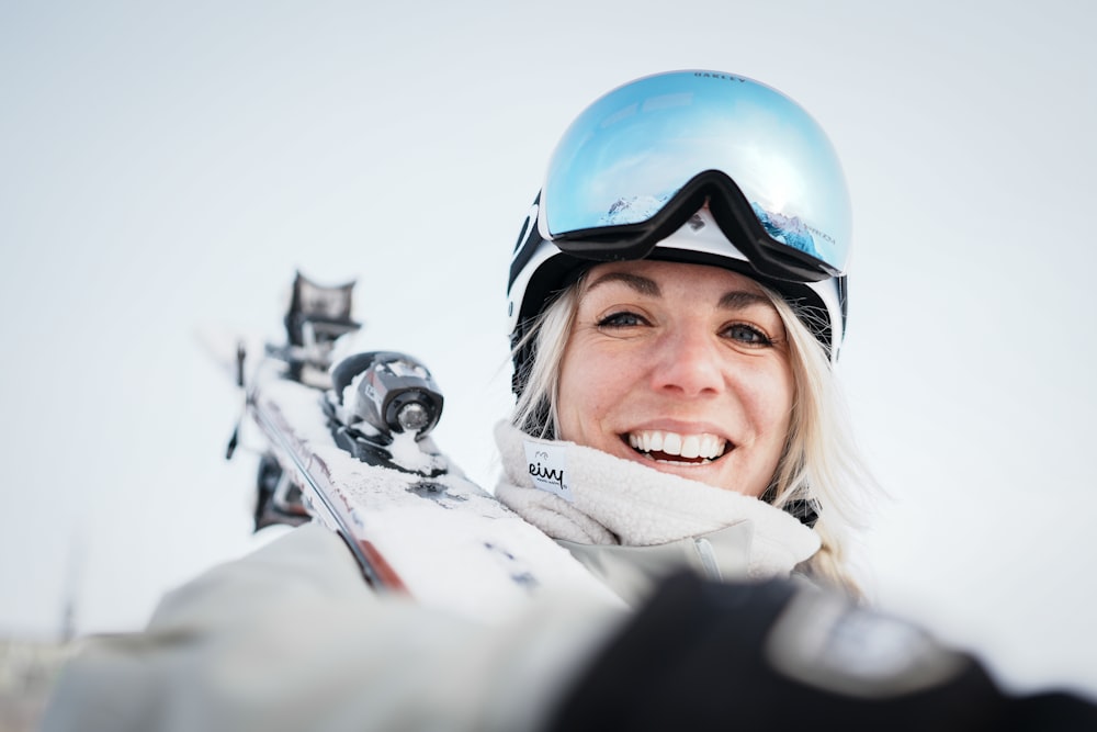 Eine Frau mit Helm und Schutzbrille hält Skier