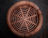 A circular woven rattan stool is seen from above, showcasing its intricate spiral design. The surrounding ground is tiled with a muted gray-blue color, adding a contrasting background to the warm brown tones of the stool.