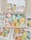 A collection of colorful, cute cartoon-like characters in pastel shades, packed inside cardboard boxes with clear lids. The characters have cheerful, smiling faces and are shaped like various animals and objects.