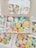 A collection of colorful, cute cartoon-like characters in pastel shades, packed inside cardboard boxes with clear lids. The characters have cheerful, smiling faces and are shaped like various animals and objects.