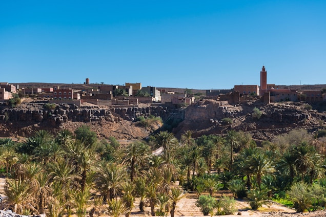 A vibrant desert landscape with film crew setting up cameras near traditional Moroccan architecture under warm sunlight.