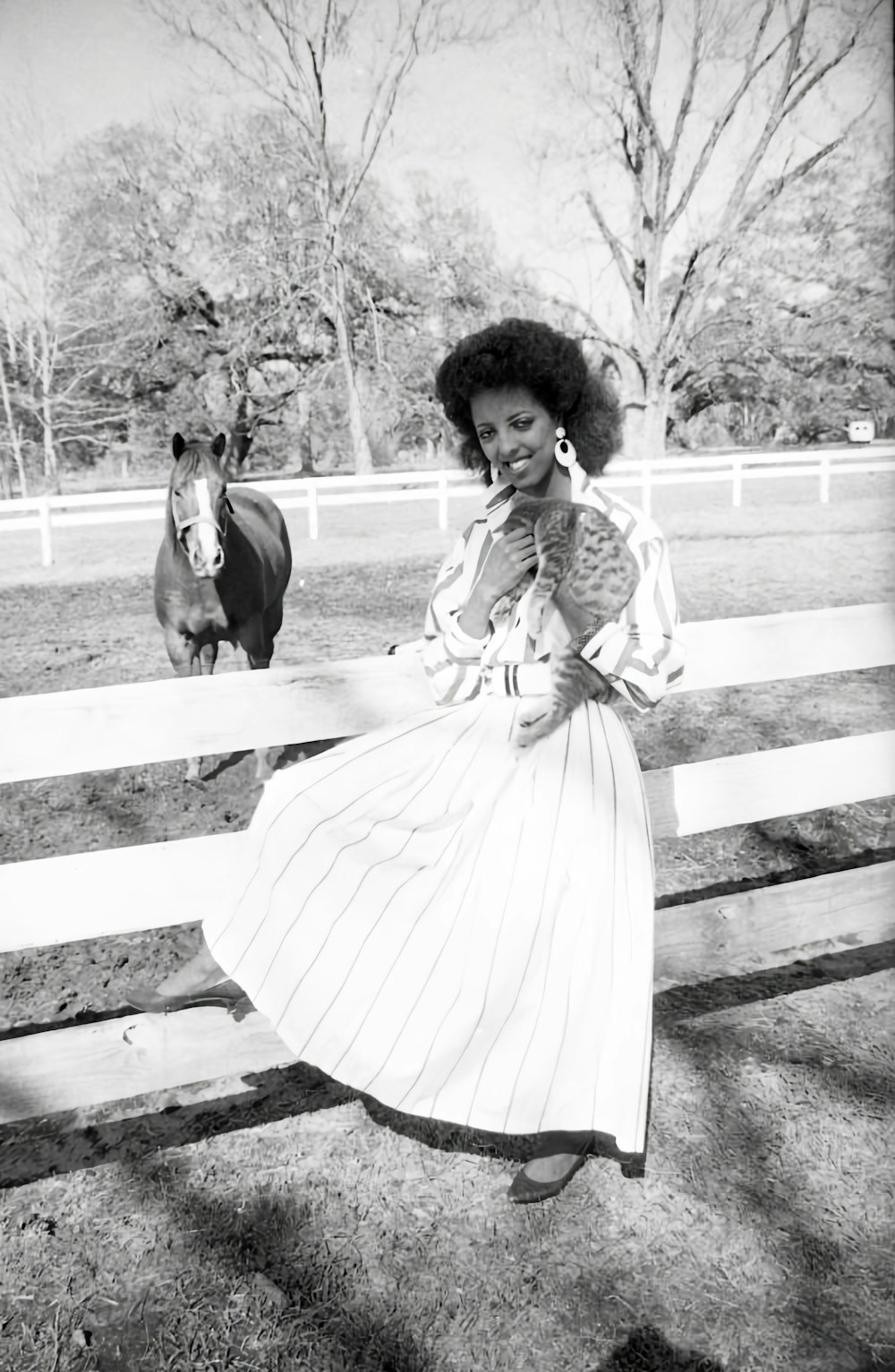 a woman standing in front of a fence next to a horse