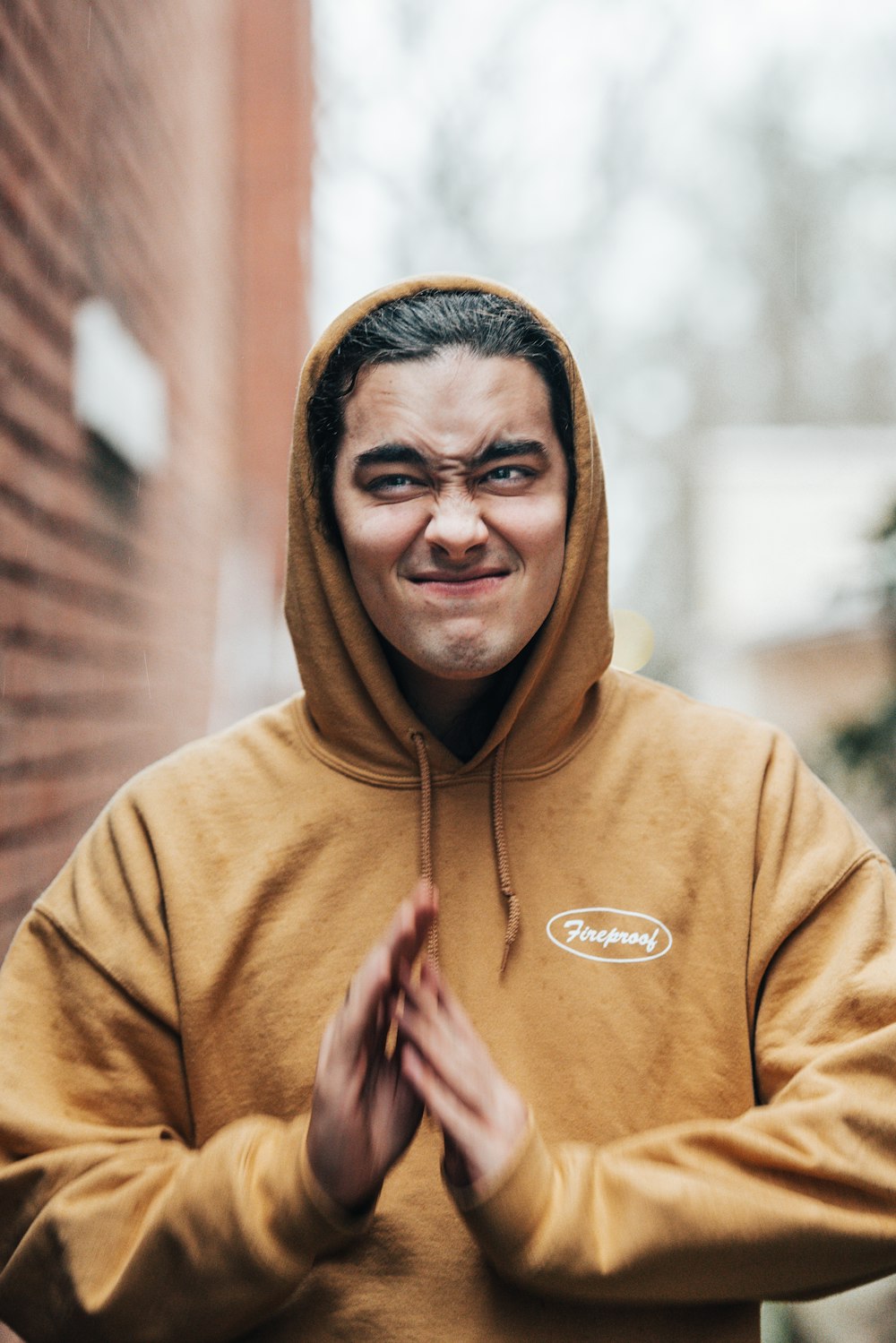 a man in a yellow hoodie standing in front of a brick wall