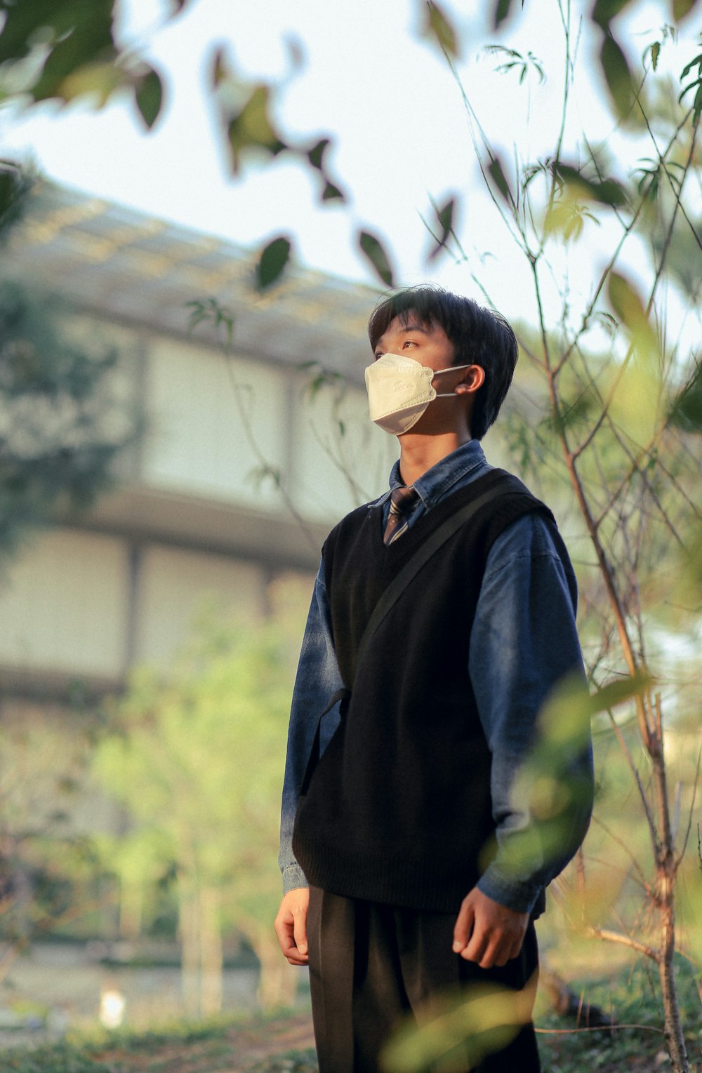 a man wearing a face mask standing next to a tree