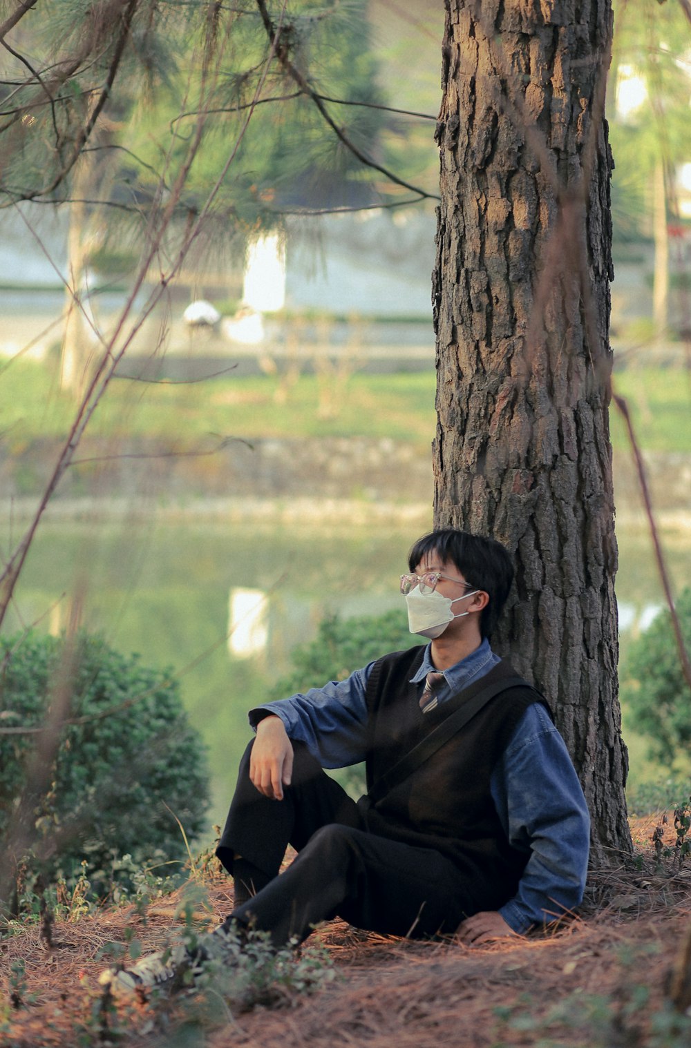 a man sitting under a tree wearing a face mask