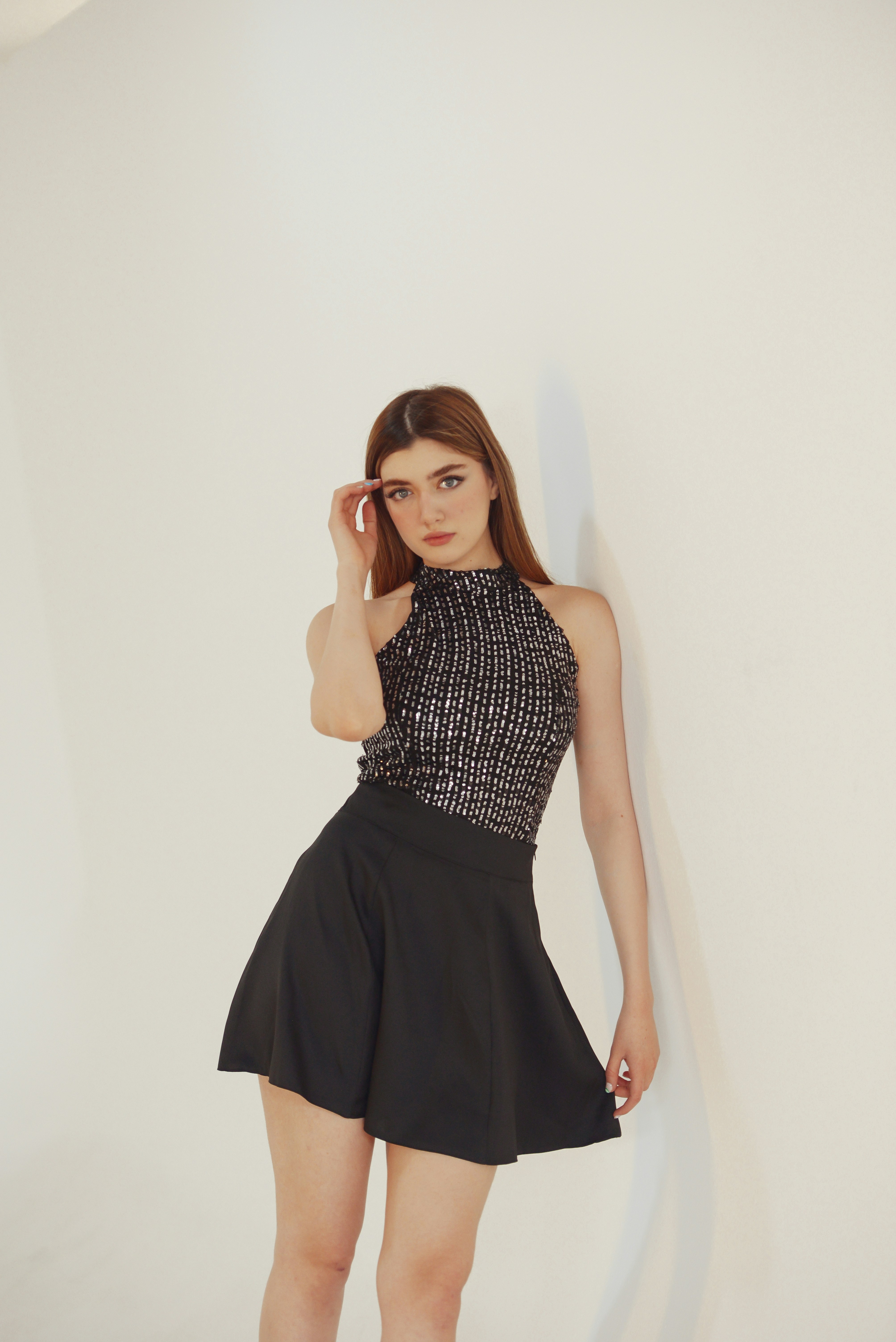 a woman in a short black dress leaning against a wall