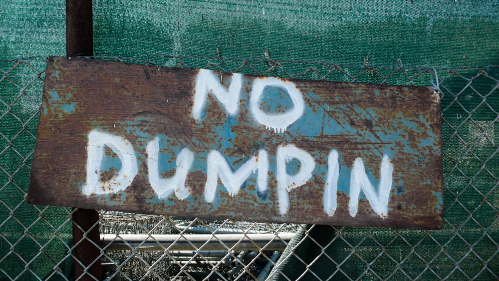 a rusted no dumping sign on a chain link fence