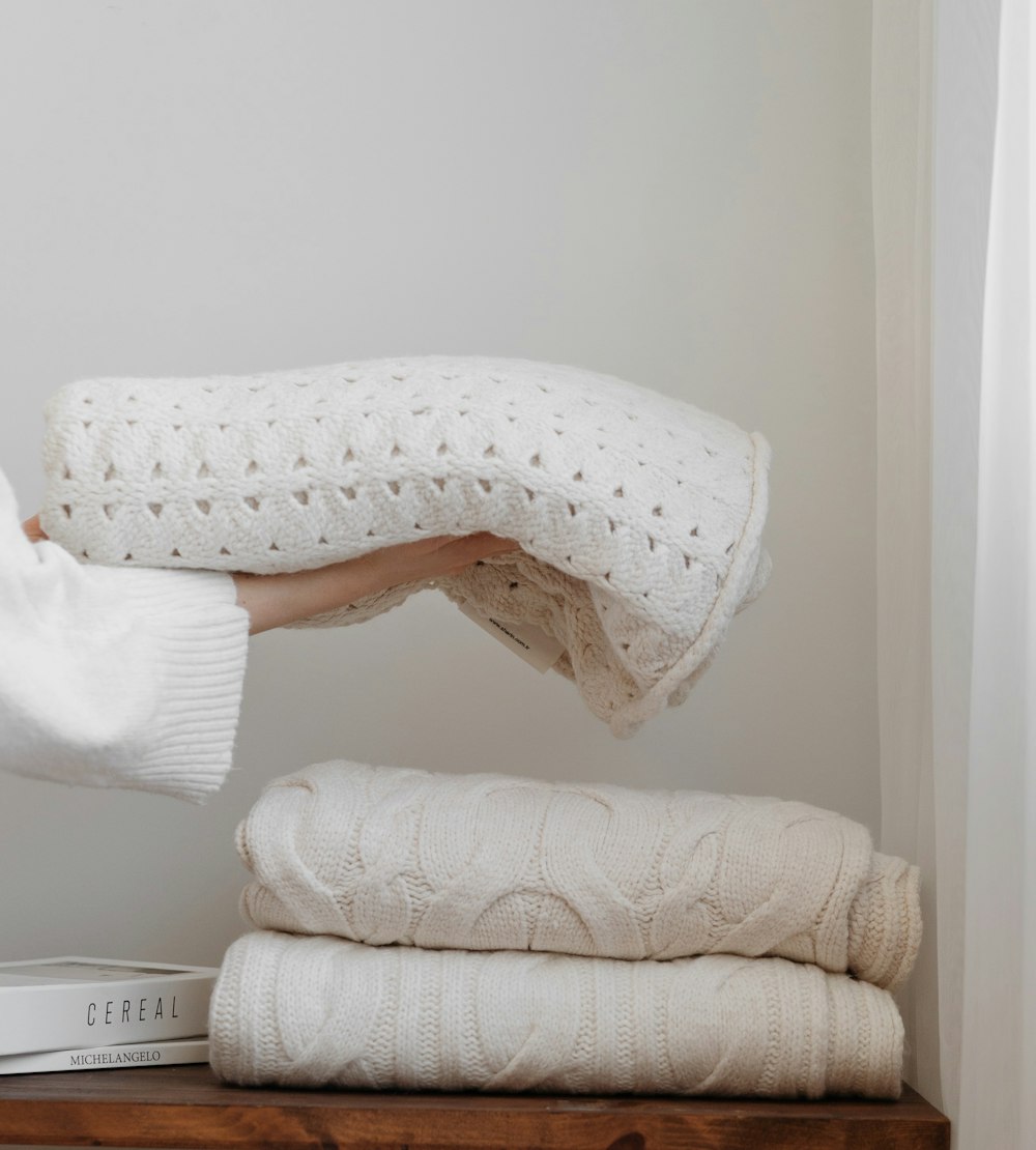 a person holding a blanket over a stack of blankets