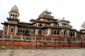 A large, ornately designed building with multiple domes and arches, featuring intricate architectural details. It is surrounded by a fence and has a sign indicating 'Tickets' at the entrance.